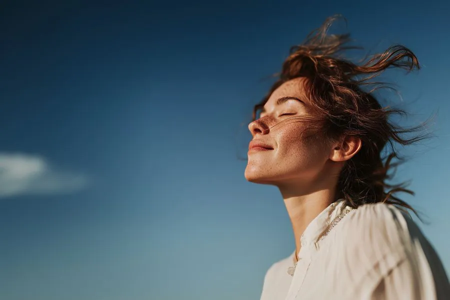A woman smiling with her eyes closed while the wind blows in her hair.